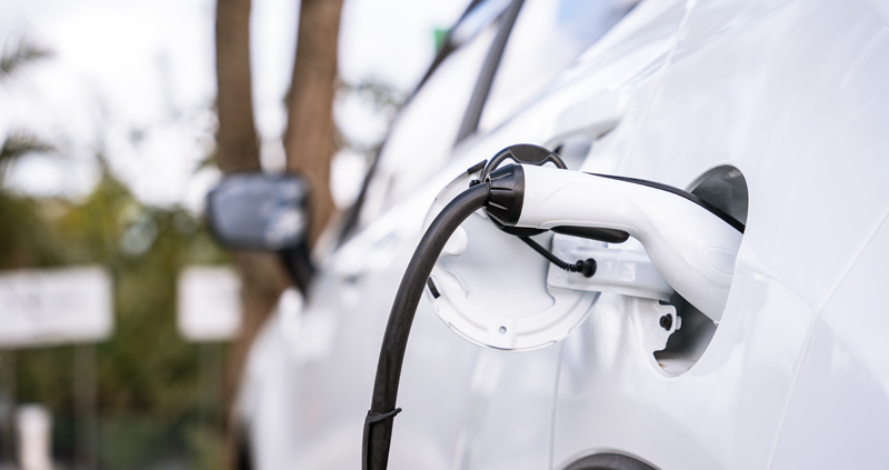 weißes Elektroauto steckt an Zapfsäule und lädt